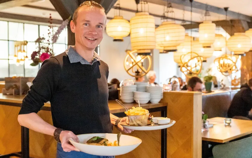 Een man houdt een bord met eten vast in een restaurant.