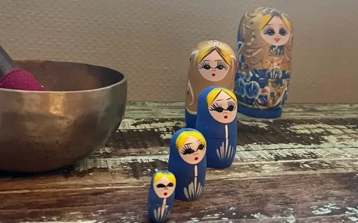 A group of nesting dolls are sitting on a wooden table next to a bowl.