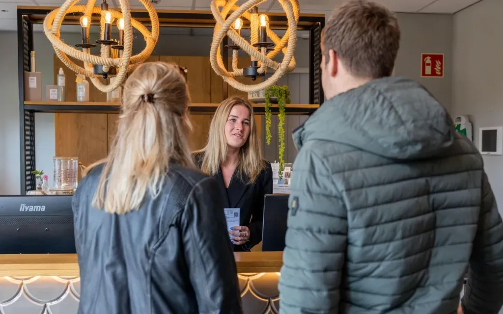 Een vrouw praat met een man en een vrouw aan de balie van een hotel.