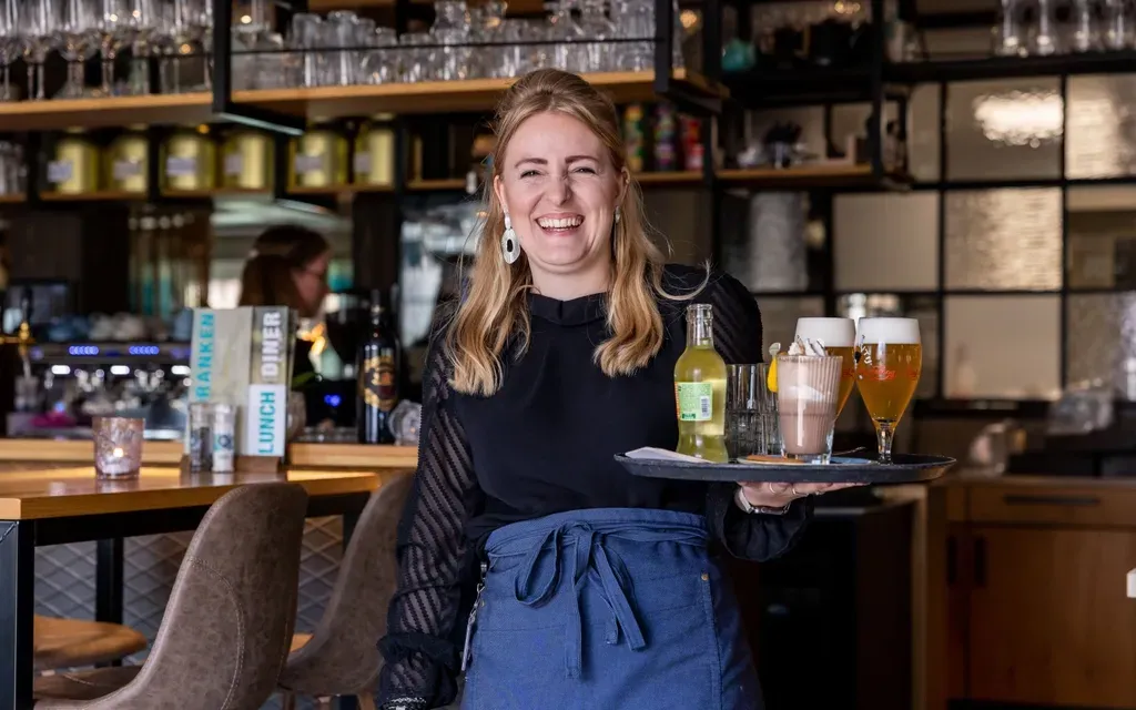 Een vrouw houdt een dienblad met drankjes vast in een restaurant.