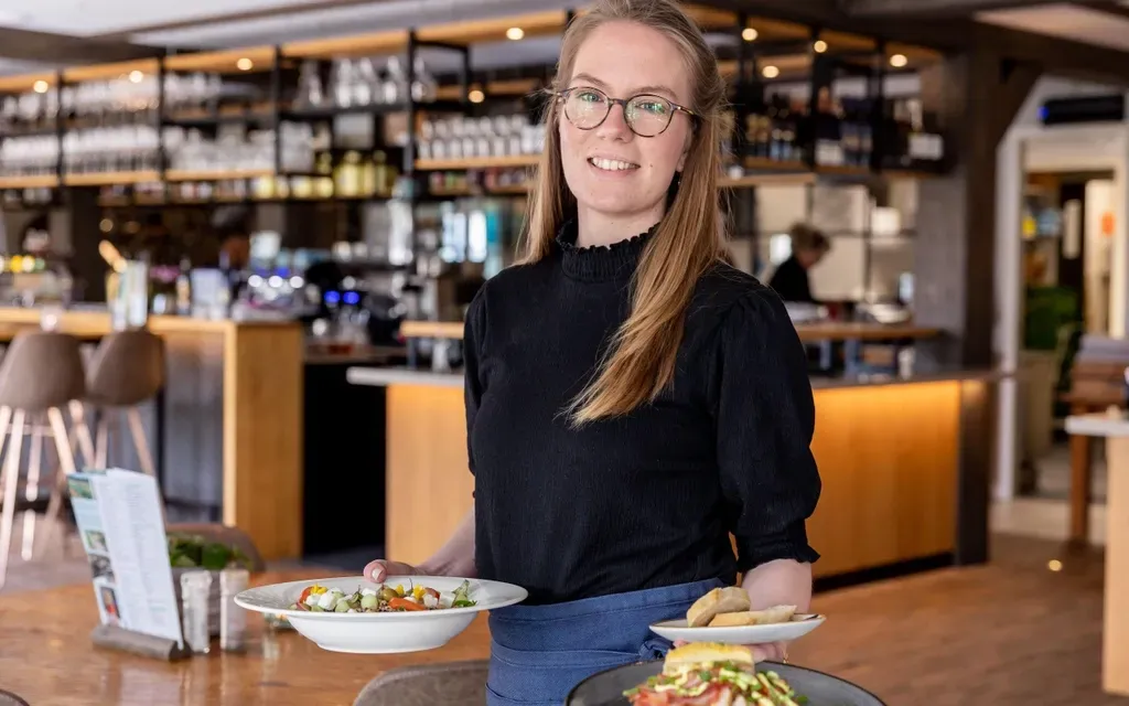 A waitress is holding two plates of food in a restaurant.