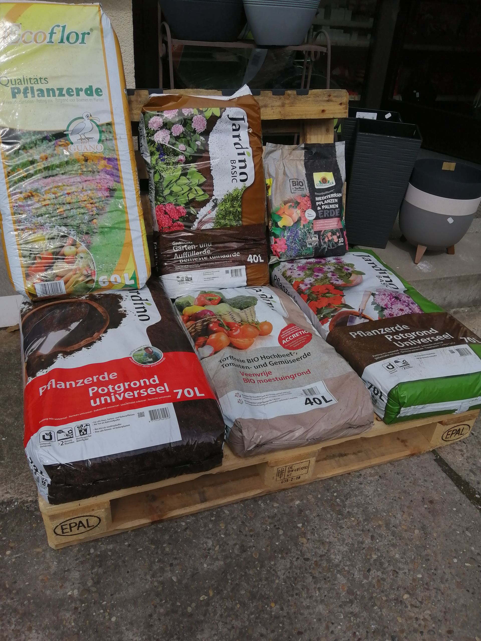 Säcke mit Gartenerde verschiedener Marken, ausgestellt auf einer Holzpalette im Freien.