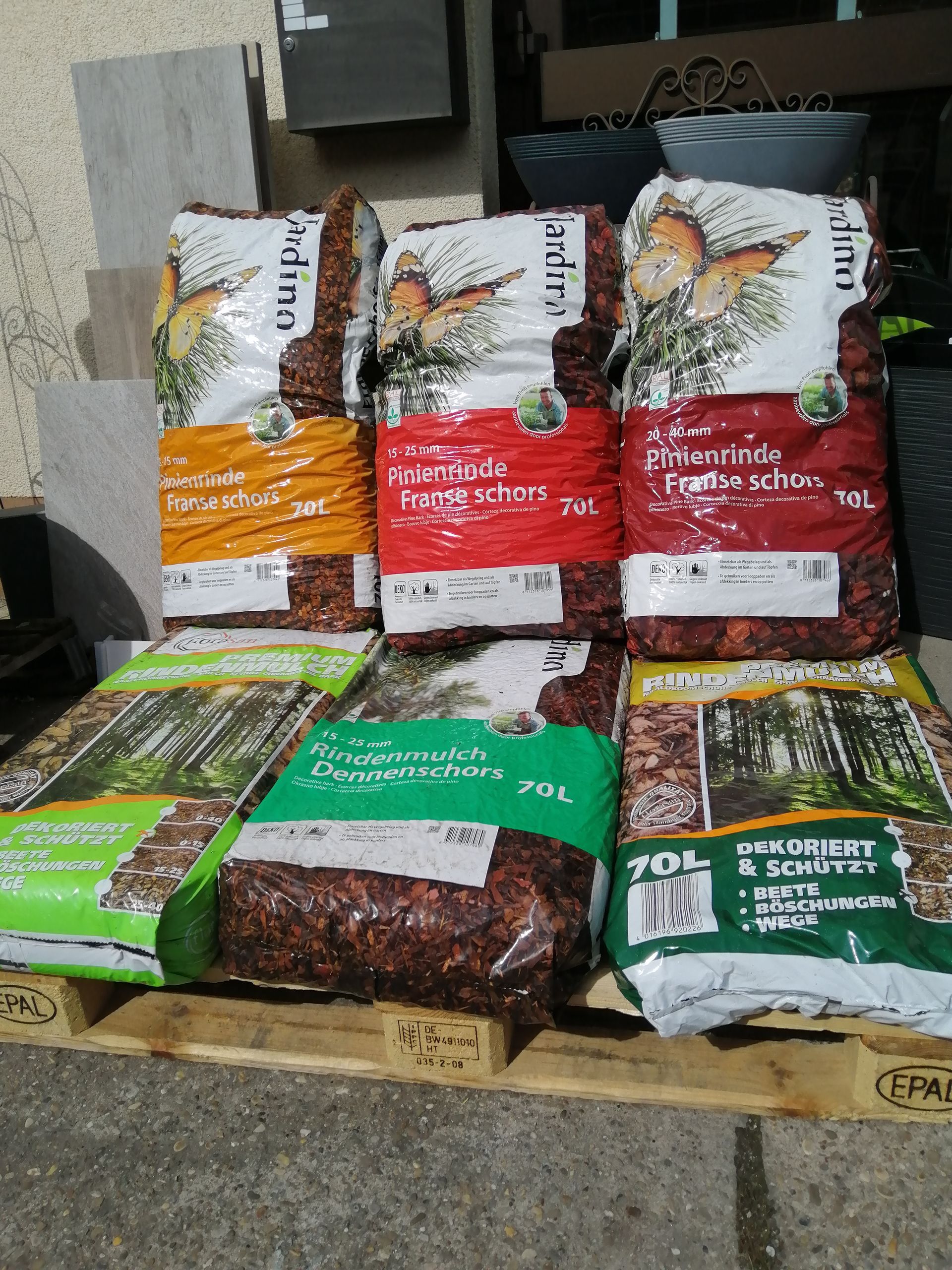 Säcke mit Mulch und Holzspänen auf einer Holzpalette. Verschiedene Farben und Marken.