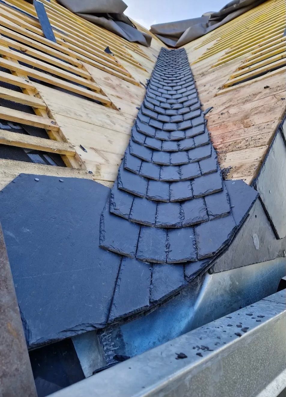 Tuiles d'ardoise bleue disposées dans une étroite noue entre les pans de toiture.