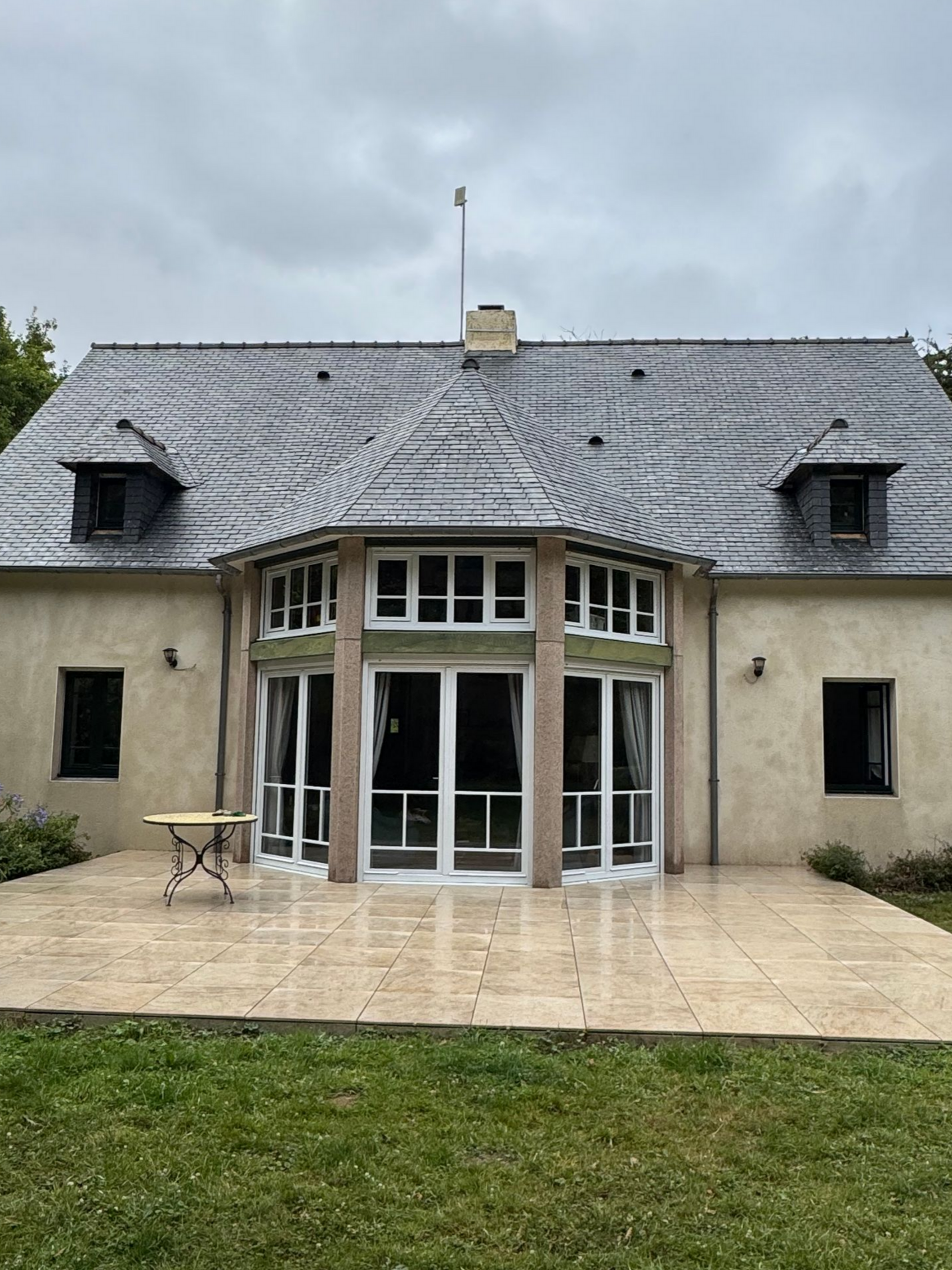 Maison en pierre avec toit en ardoise grise, grandes portes vitrées et patio.