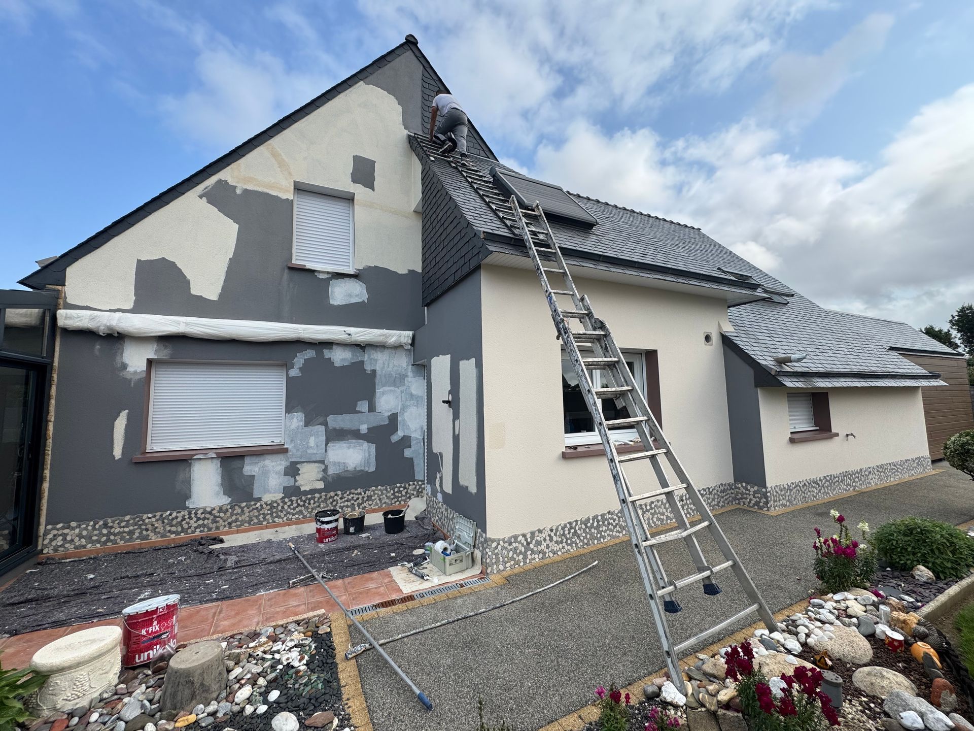 Façade de la maison avec des retouches de peinture fraîche et des échelles pour les réparations du toit et des murs.