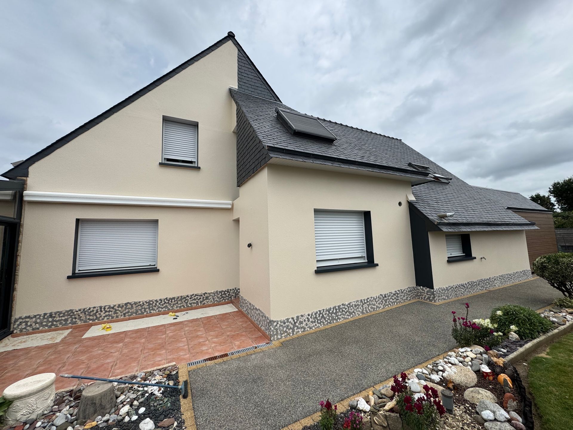 Maison moderne couleur crème avec toit gris foncé, fenêtres à volets.