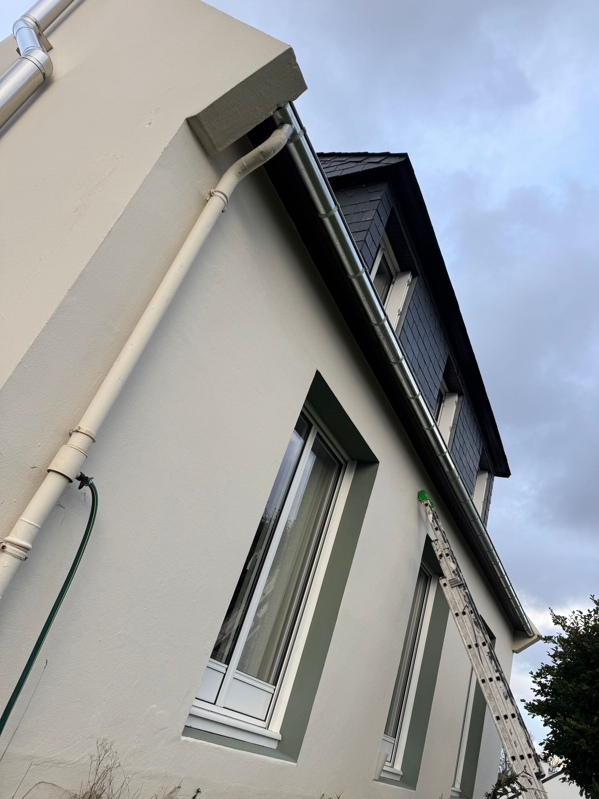 Une maison beige aux fenêtres encadrées et au toit en ardoise.