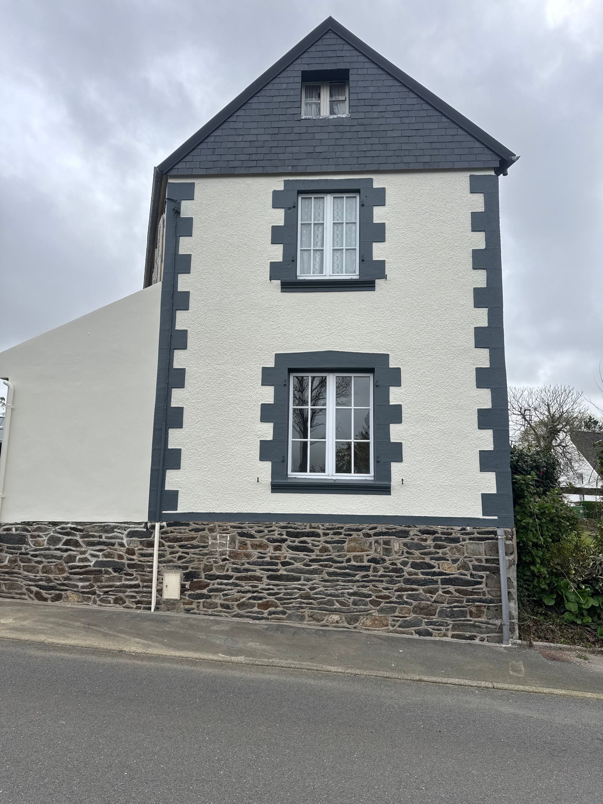 Maison en pierre blanche avec toit en ardoise sombre et soubassement en pierre.