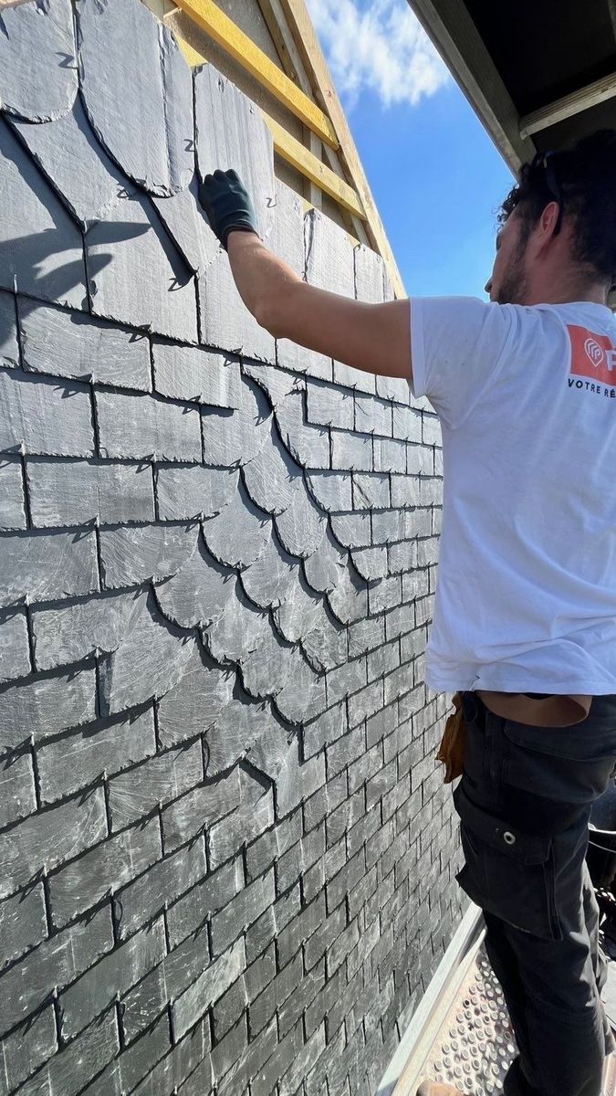 Un ouvrier recouvre le mur d'une maison d'ardoise.