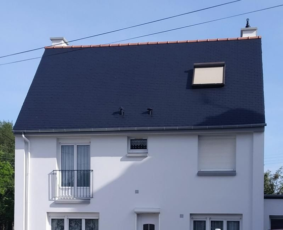 Maison blanche au toit bleu foncé pentu, lucarne, balcon et volets fermés.