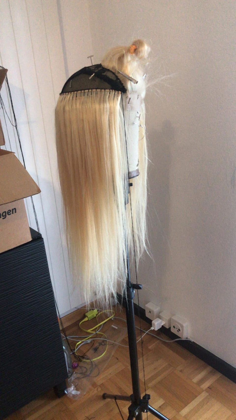 Eine lange, blonde Perücke auf einem Ständer, wahrscheinlich zum Stylen im Innenbereich.
