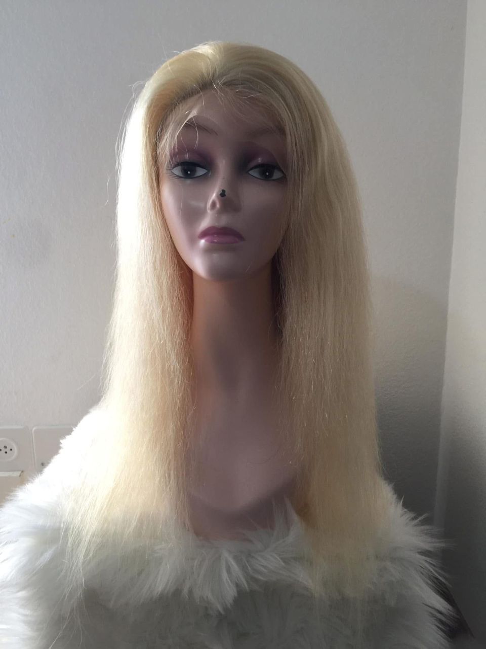 Blonde Perücke auf einem Schaufensterpuppenkopf; glattes, strukturiertes Haar, blasse Haut, weißer Pelzkragen.