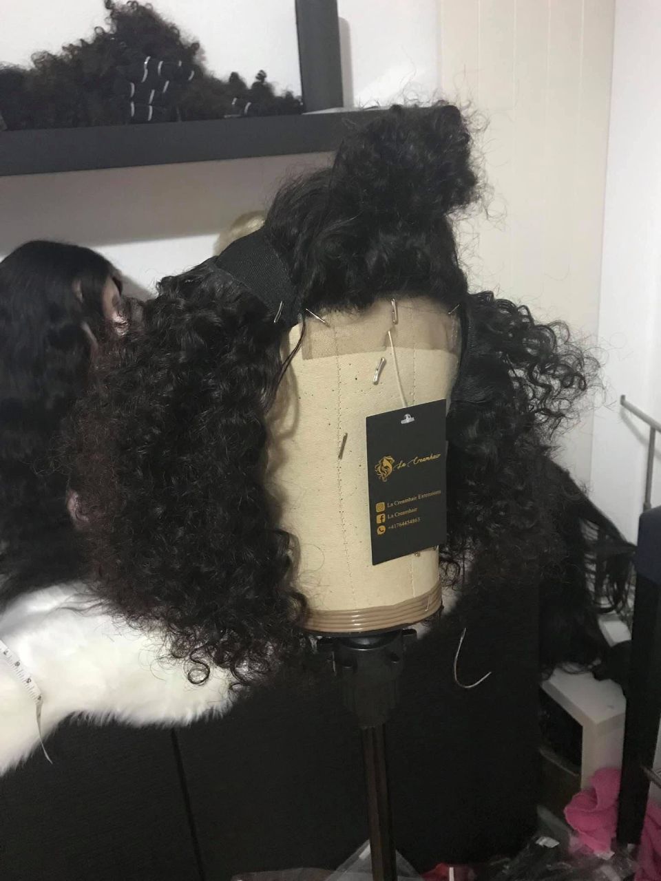 Eine lockige schwarze Perücke auf einem Schaufensterpuppenkopf mit einem daran befestigten Etikett auf einem Ständer.