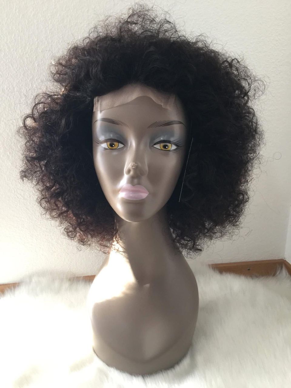 Schaufensterpuppenkopf mit einer lockigen schwarzen Perücke, der auf einer weißen, flauschigen Oberfläche ruht.
