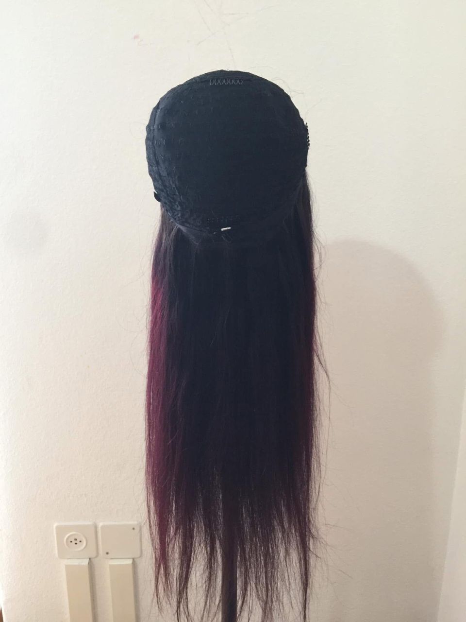 Perücke auf einem Ständer mit langen, dunklen Haaren, die an den Enden in ein Rotviolett übergehen.