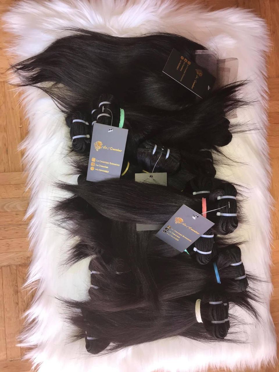 Schwarze Haarverlängerungen auf einem weißen Fellteppich, an einigen Bündeln sind Produktetiketten angebracht.