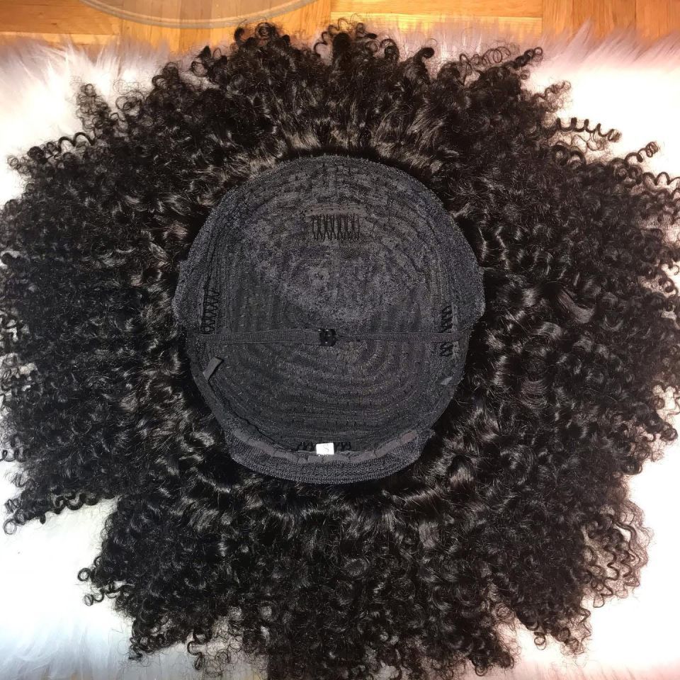 Schwarze Afroperücke mit dunkler Kappe auf weißem Felluntergrund.