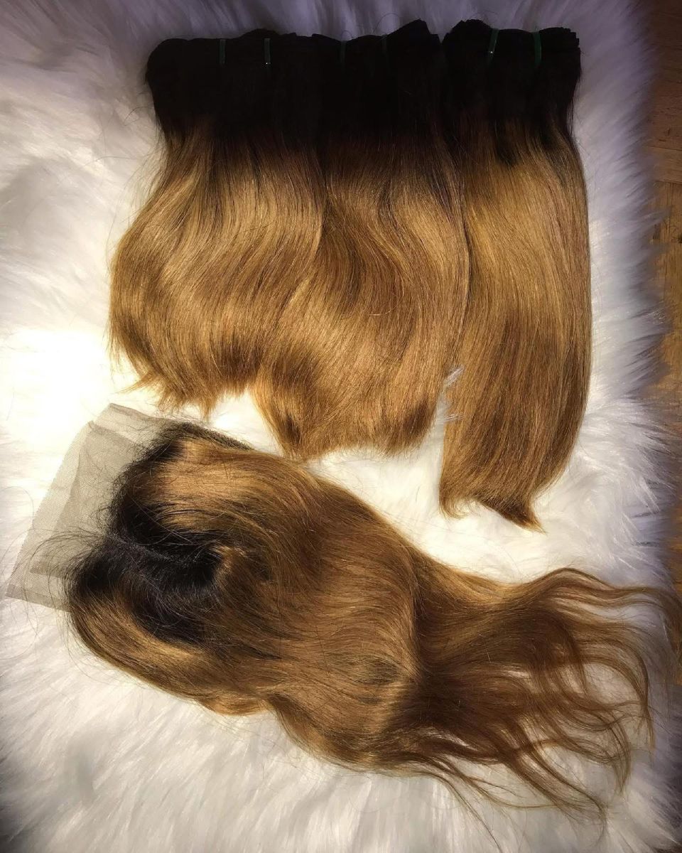 Bündel aus Ombre-braunem bis goldblondem Haar mit Spitzenverschluss auf weißem Fell.