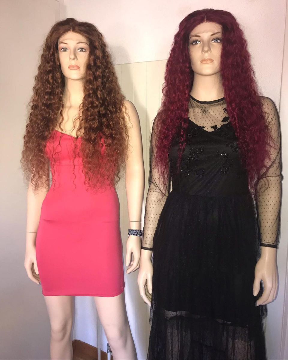 Zwei Schaufensterpuppen mit lockigen Perücken; eine in einem roten Kleid, eine in einem schwarzen Kleid. Drinnen.