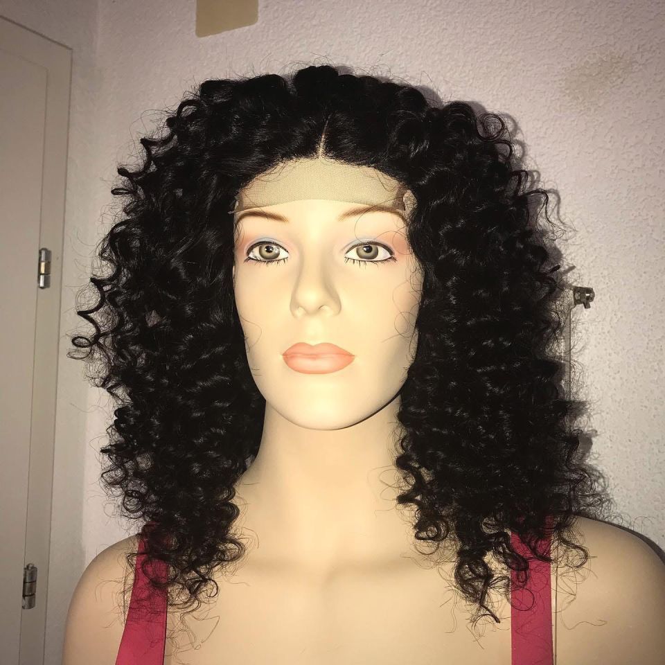 Schaufensterpuppe mit dunkler Lockenperücke und rötlich-rosa Oberteil; schlichter weißer Wandhintergrund.