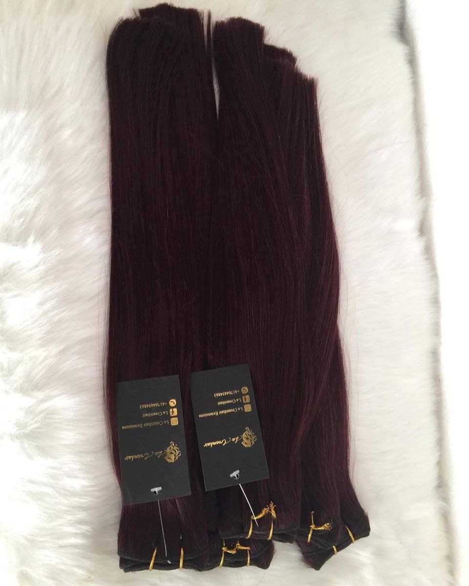 Bündel dunkelroter Haarverlängerungen auf einer weißen Felloberfläche mit daran befestigten Produktetiketten.