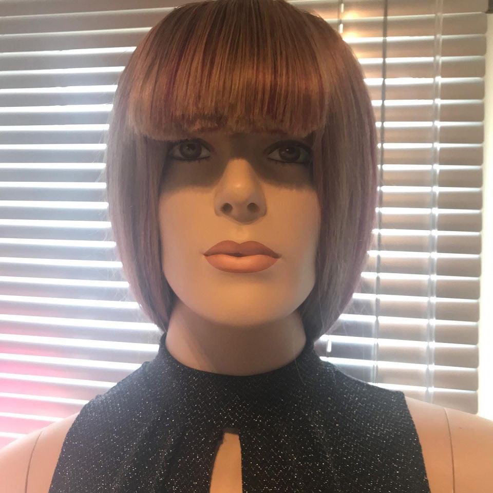 Schaufensterpuppenkopf mit Perücke, rotbraunem Haar, Pony und schwarzem Glitzeroberteil vor Jalousien.