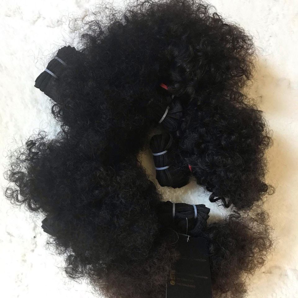 Bündel dunkler, eng gelockter Haarverlängerungen, mit Gummibändern und Papieretiketten zusammengebunden.