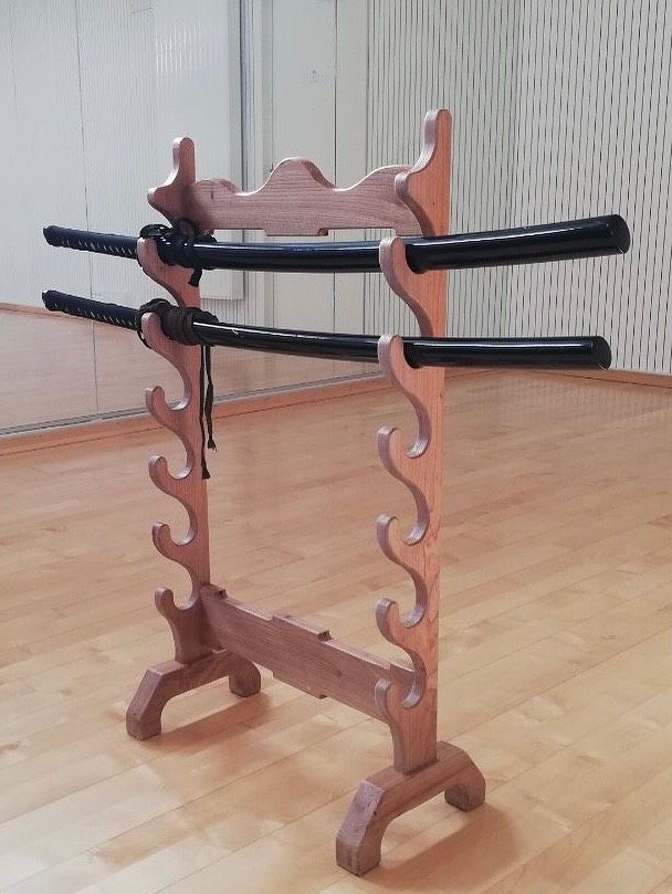 Râtelier à épées en bois avec des épées à manche noir sur un parquet.