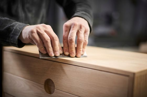 Des mains qui poncent un tiroir en bois clair avec du papier de verre