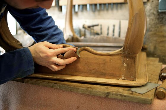 Des mains ponçant un cadre de chaise en bois dans un atelier