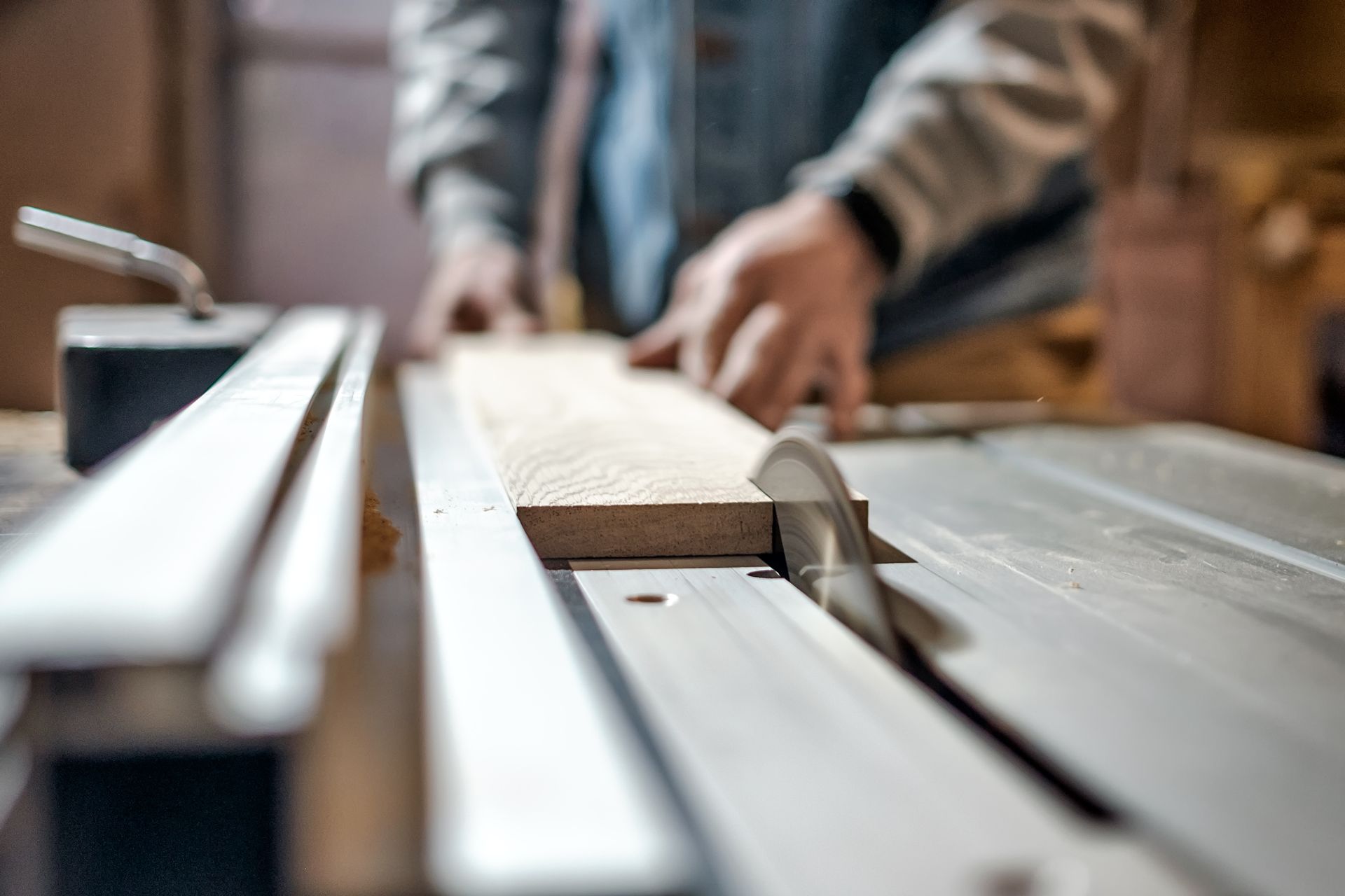 Des mains guidant du bois à travers une scie circulaire dans un atelier