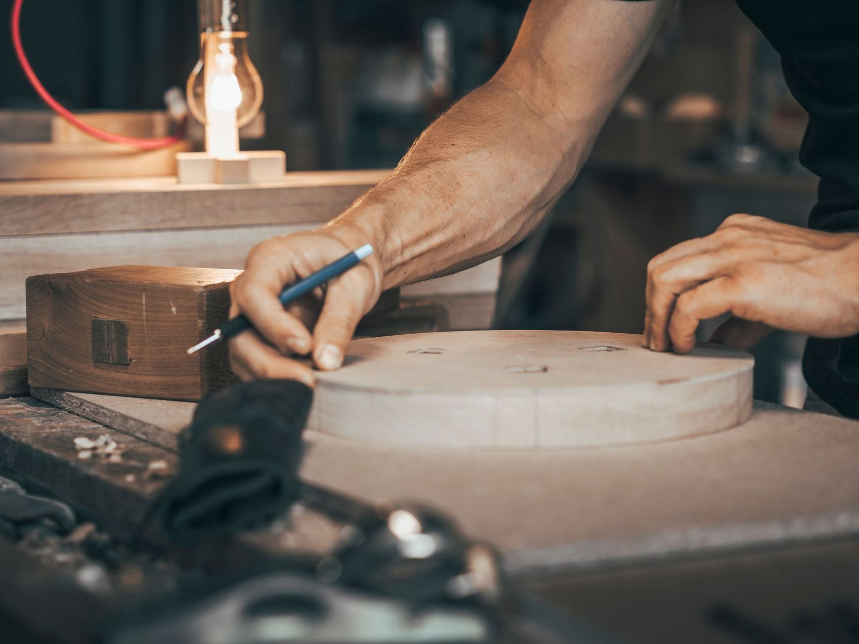 Des mains sculptent un bol en bois sur un tour dans un atelier, avec des outils à proximité.