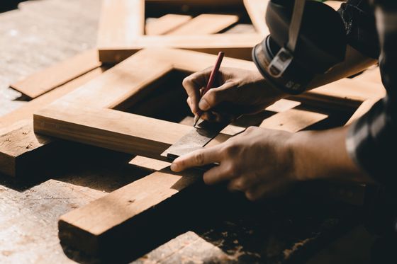 Des mains mesurant une planche de bois avec un crayon sur un établi de menuisier