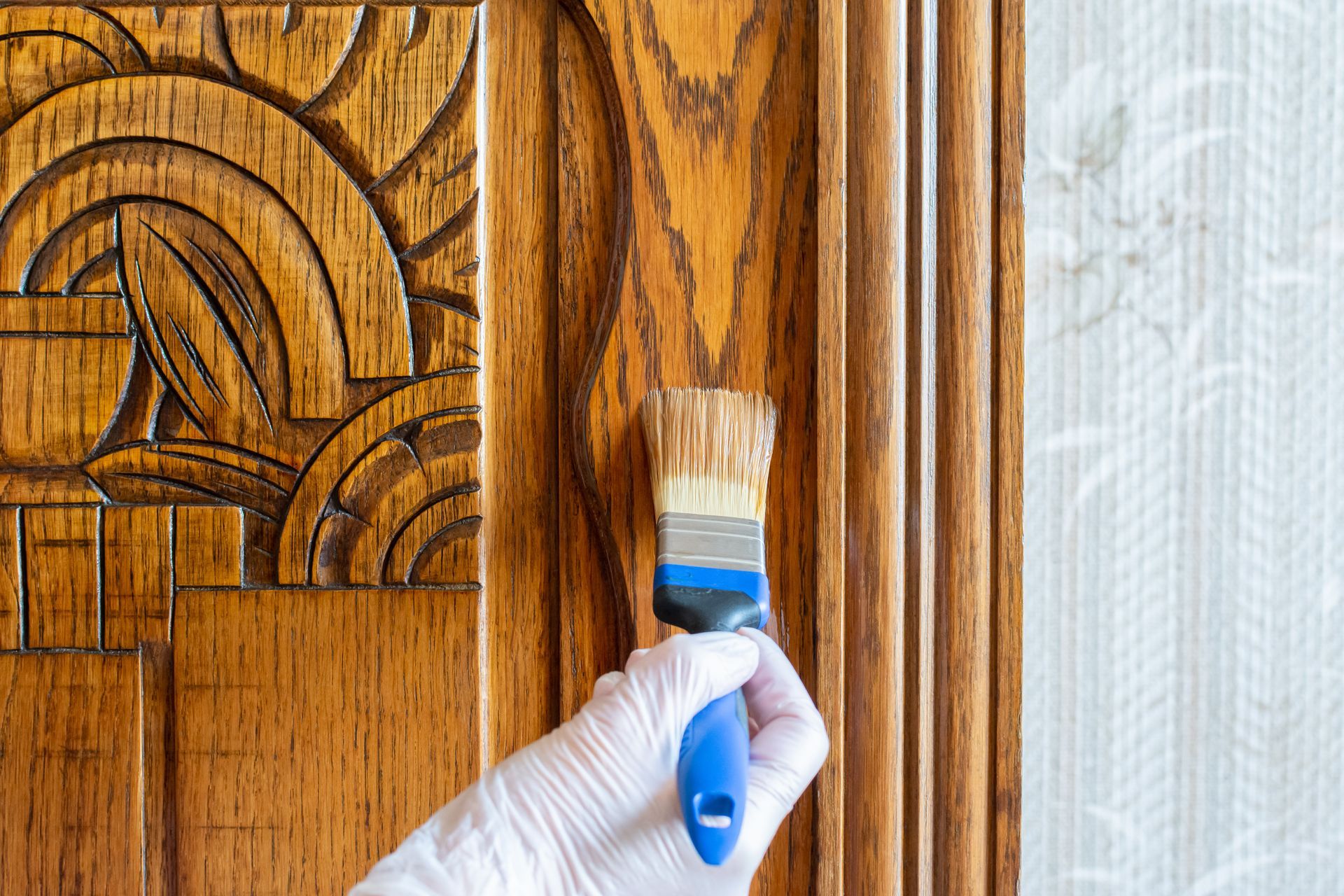 Main gantée peignant un panneau de porte en bois sculpté avec un pinceau bleu
