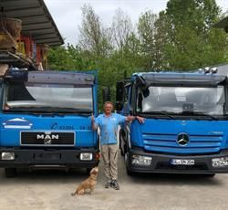 Ein Mann und ein Hund stehen vor zwei blauen Lastwagen.