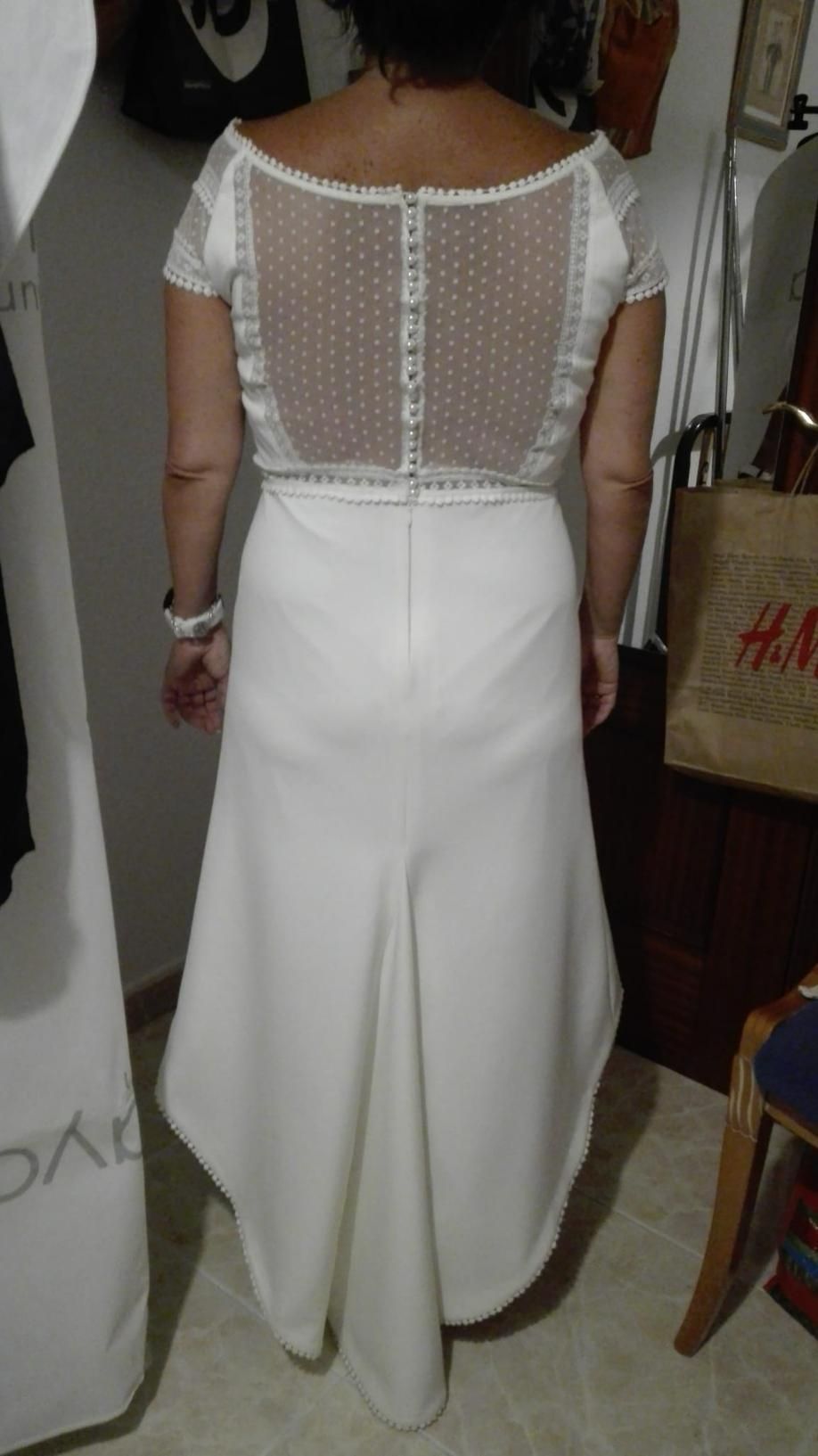 Mujer con un vestido blanco con lunares transparentes en la espalda, de pie en el interior.