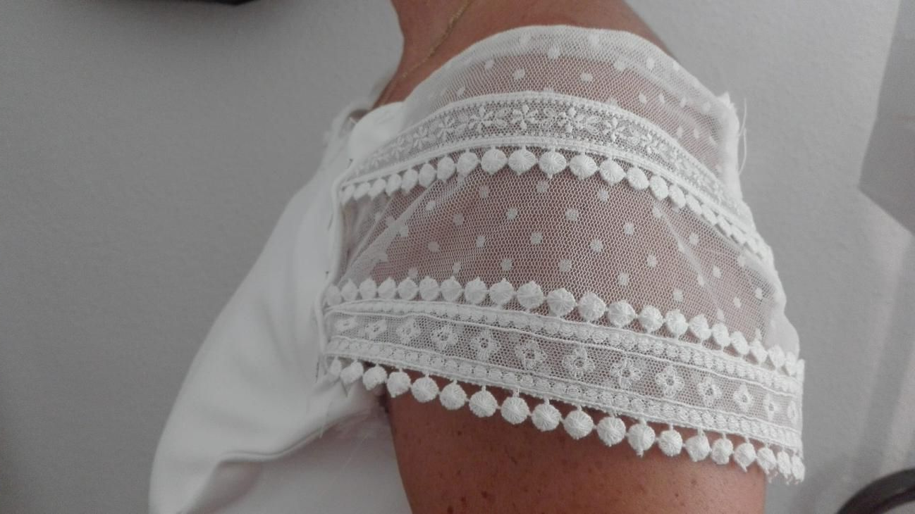 Manga de encaje blanco con ribete de pompón en un brazo.