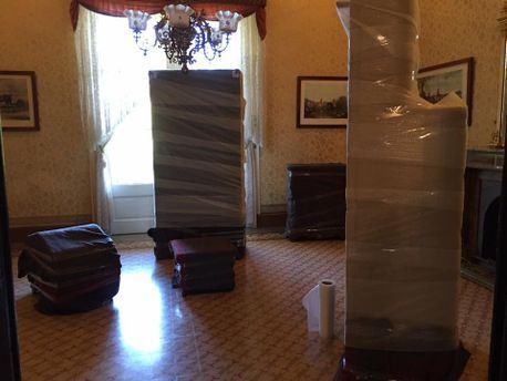 Habitación con muebles envueltos para mudanza, incluidas columnas altas y elementos apilados.