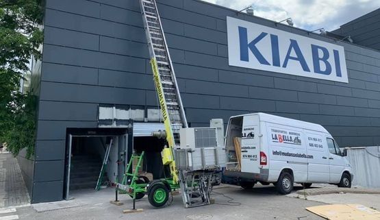 Un camión de servicio con plataforma elevadora está estacionado afuera de una tienda Kiabi.