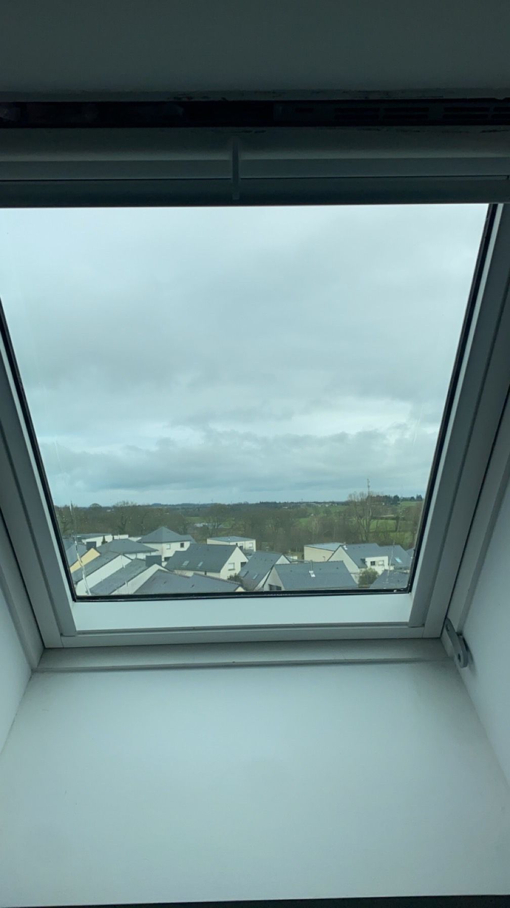 Vue de maisons et d'un ciel nuageux à travers une lucarne à cadre blanc.