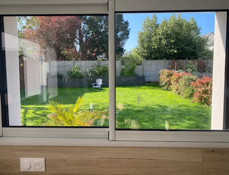 Vue d'un jardin à travers une baie vitrée coulissante. 