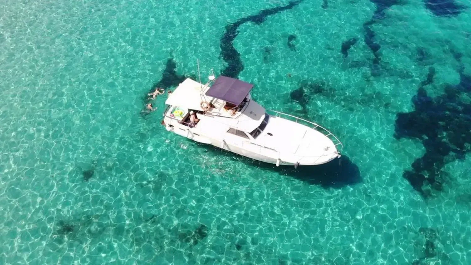 Un barco blanco flota en aguas cristalinas de color turquesa sobre parches de coral oscuro.