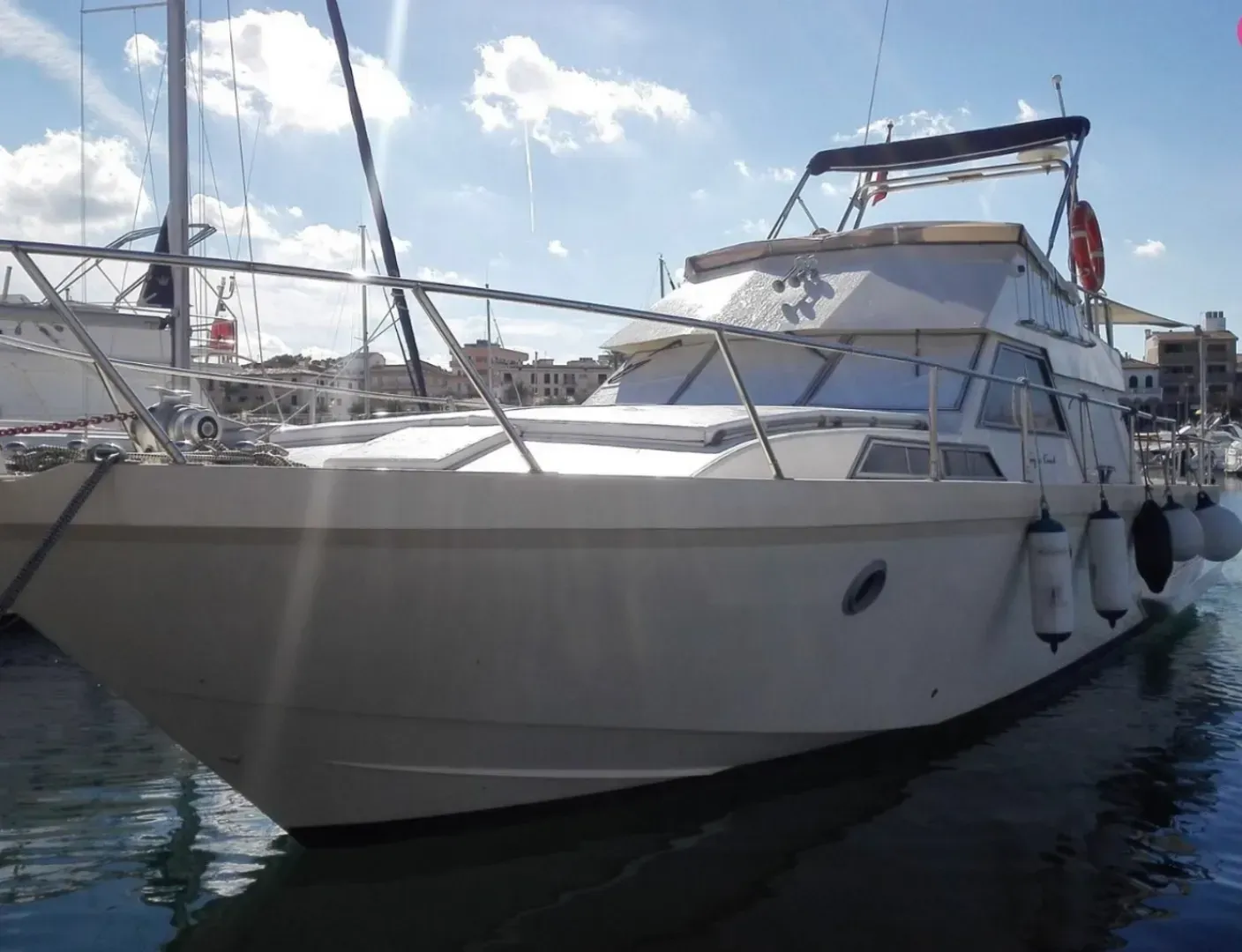 Yate blanco atracado en el puerto deportivo, visto desde la proa bajo un cielo parcialmente nublado.