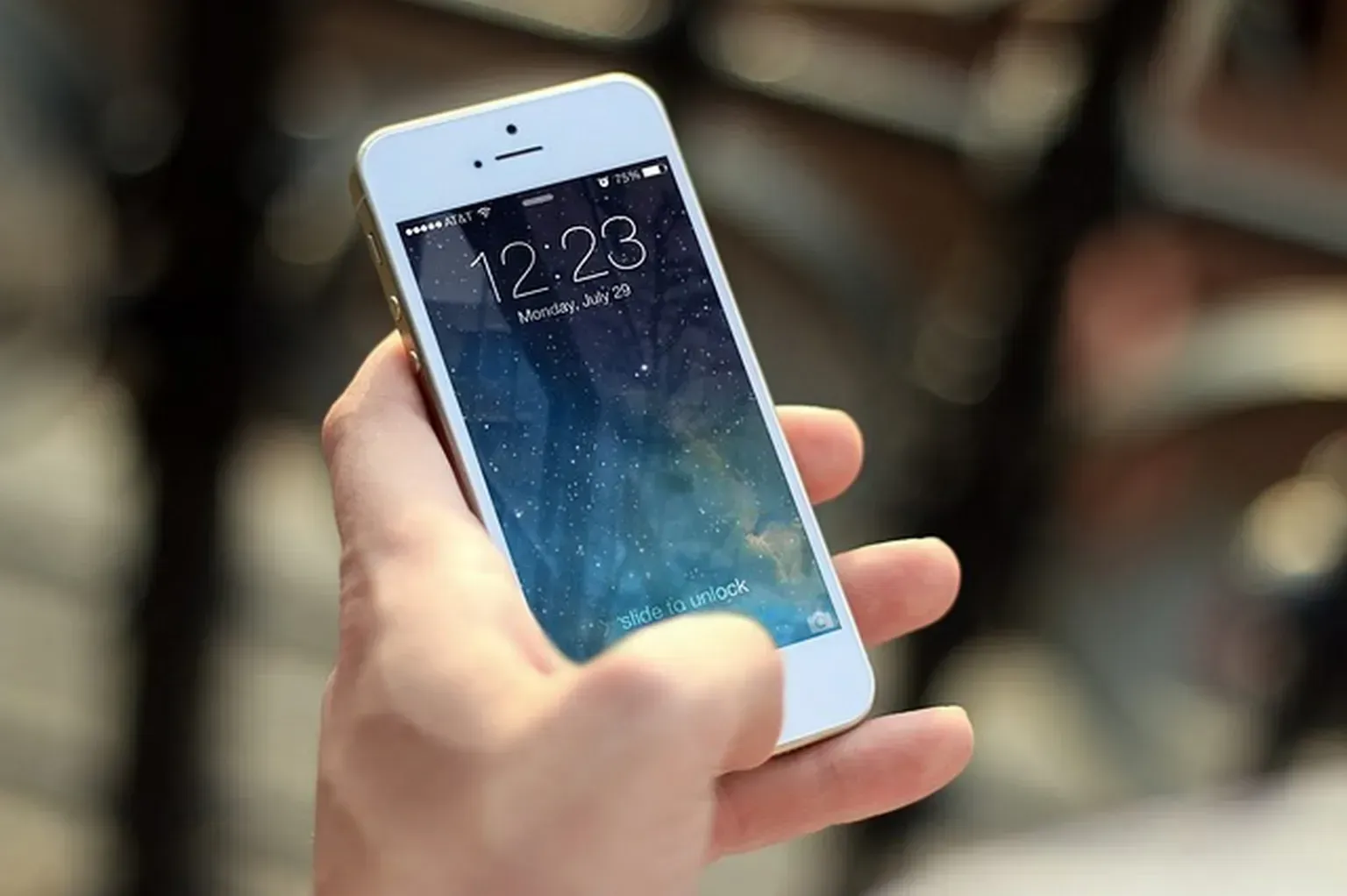 Mano sosteniendo un teléfono inteligente blanco con la pantalla de bloqueo mostrando las 12:23.