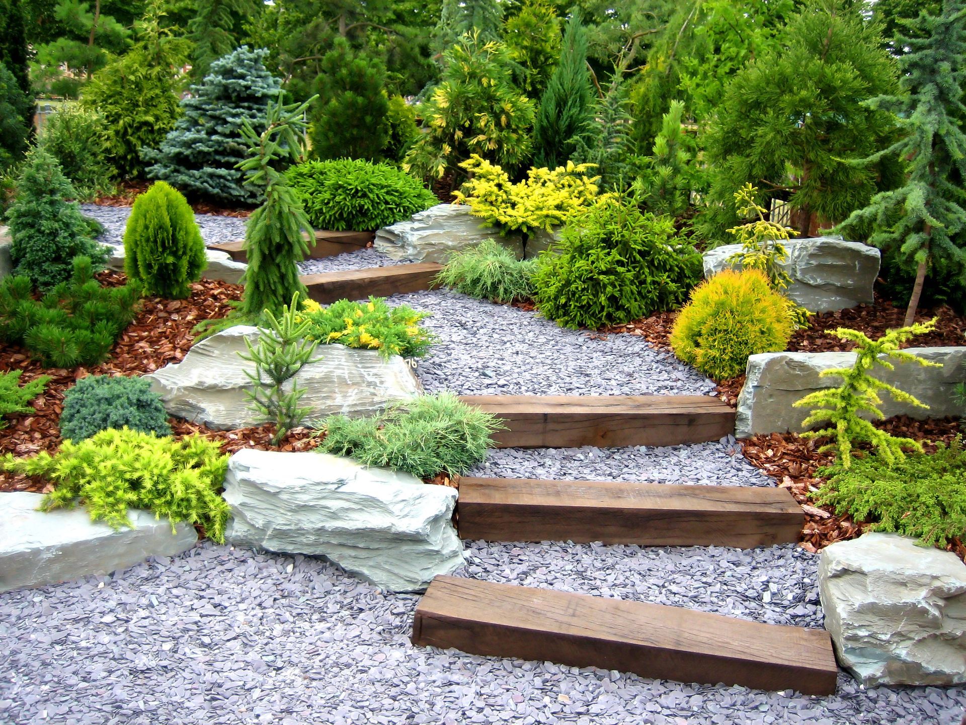 Un escalier en bois dans un jardin entouré de rochers et de plantes.