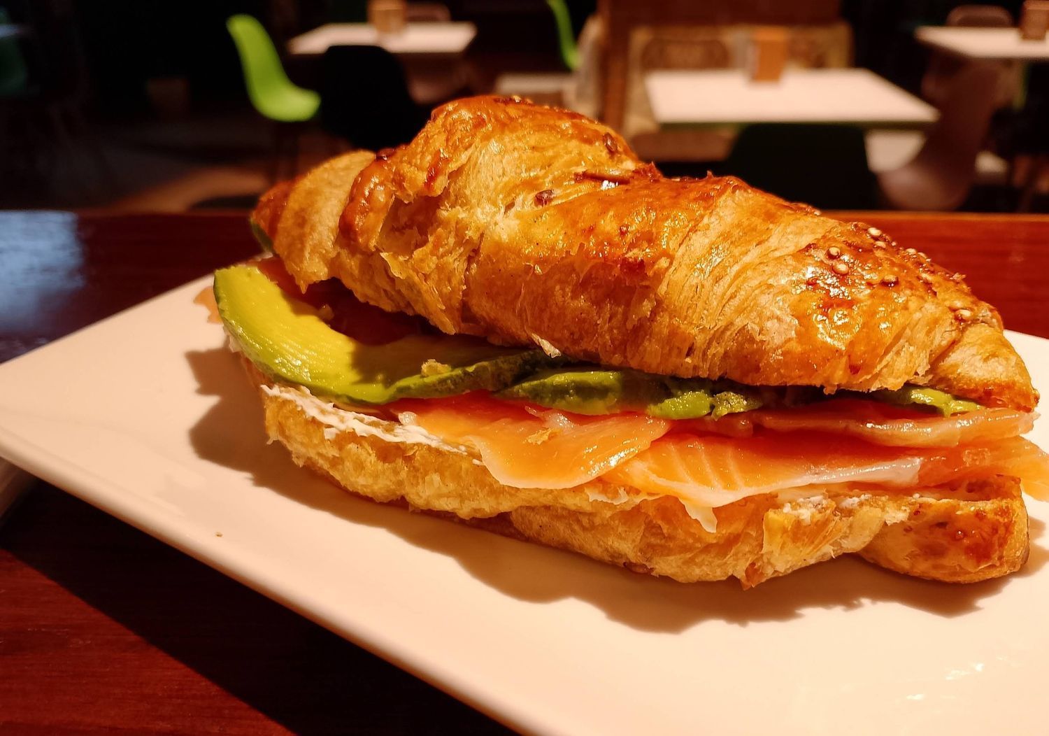 Un sándwich con aguacate y salmón ahumado sobre un croissant en un plato blanco.
