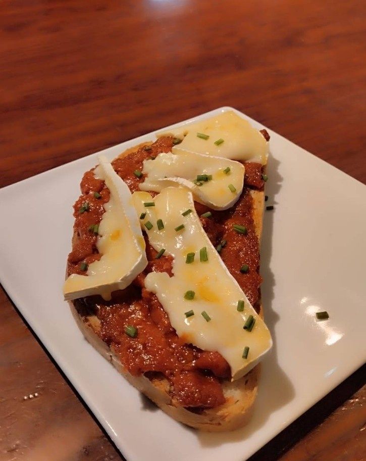 Un plato blanco cubierto con un sándwich con queso y salsa de tomate.