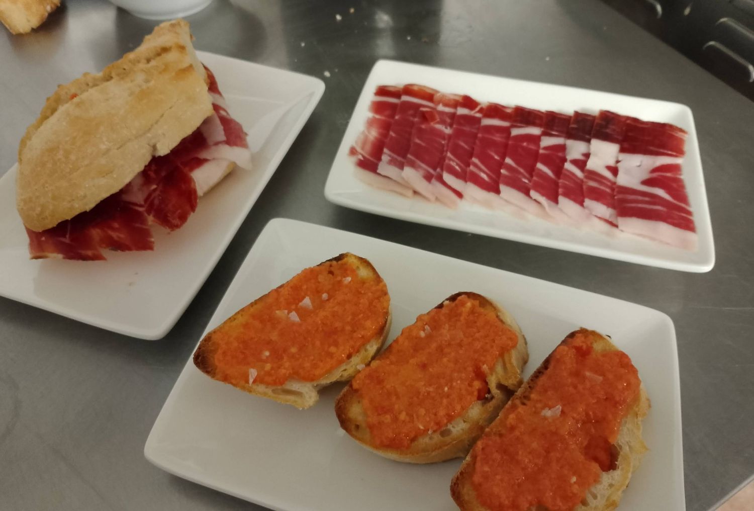 Tres platos de comida en una mesa, incluido un sándwich y un plato de carne.