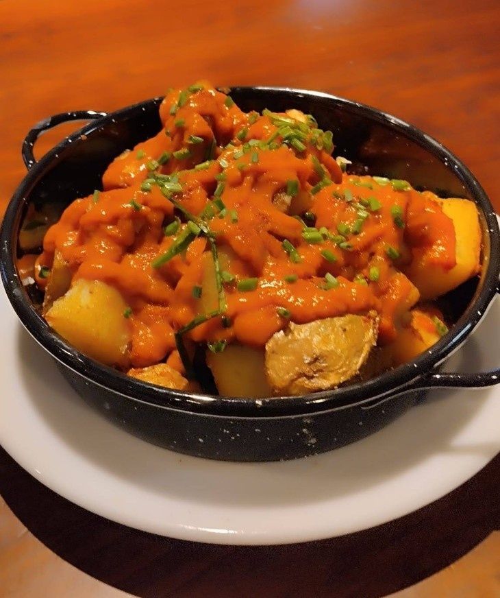 Un recipiente negro lleno de patatas y salsa en un plato blanco.